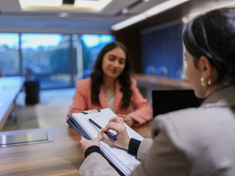 Na imagem, vemos uma cena que pode representar um atendimento em uma clínica médica ou psicológica, embora o ambiente também tenha características corporativas. A atmosfera é profissional e organizada, sugerindo um momento de entrevista, consulta ou triagem.
