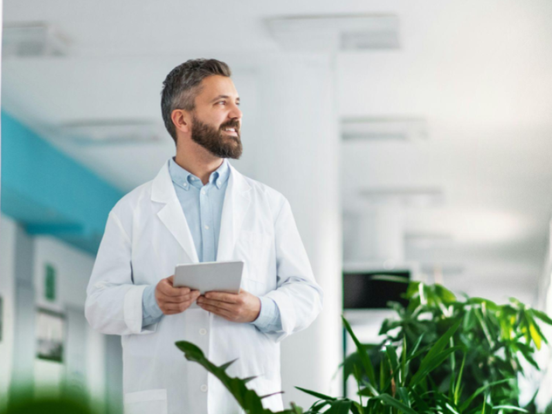 Médico em ambiente hospitalar utilizando um tablet para analisar informações clínicas e dados de pacientes, representando o uso de tecnologia na gestão de sistemas de saúde e na rotina médica sem interrupção da operação.