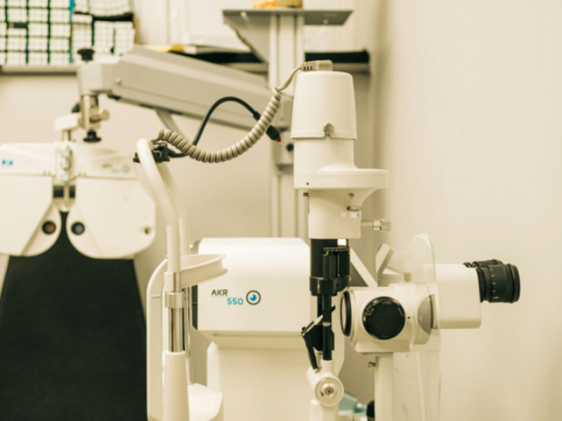 A imagem mostra o interior de um consultório oftalmológico ou optometria, equipado com instrumentos profissionais para exames de vista.