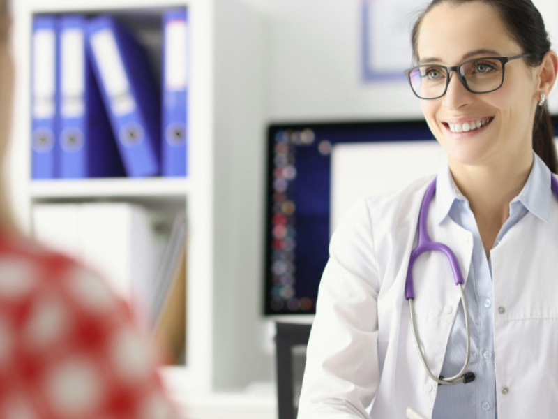 A imagem mostra uma profissional da área da saúde, provavelmente uma médica, em um consultório.