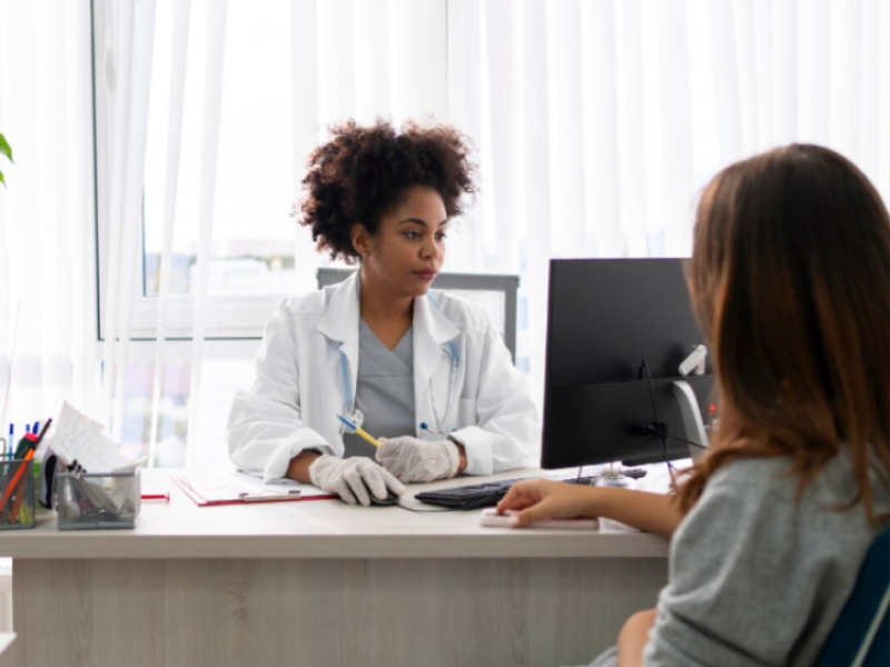 A imagem retrata um cenário de atendimento médico ou consulta clínica, destacando a interação profissional e humanizada entre uma médica e sua paciente.