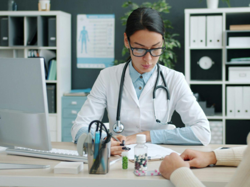 A imagem mostra uma consulta médica em um consultório bem iluminado e organizado.