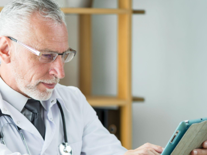 A imagem mostra um médico sênior concentrado enquanto utiliza um tablet.