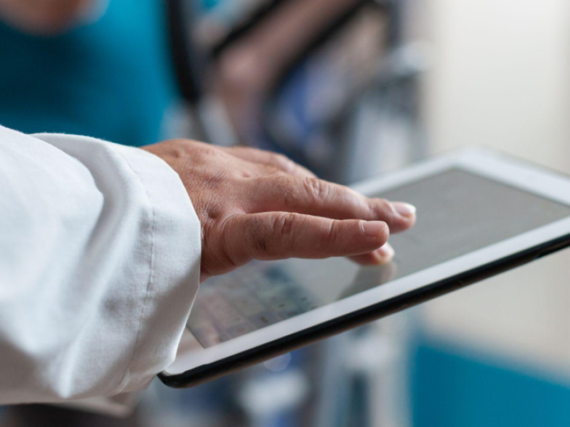 A imagem mostra um close-up de uma mão tocando a tela de um tablet, sugerindo o uso de tecnologia em um contexto profissional de software médico.