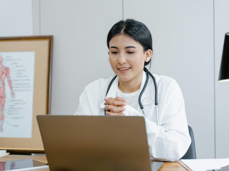 Médico em um consultório com um laptop, sugerindo o uso de uma agenda médica.