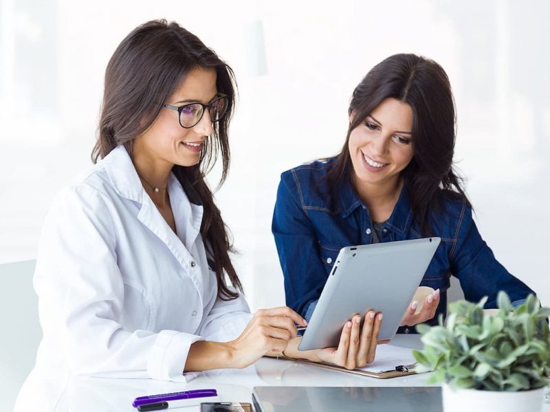 Médica segurando um tablet enquanto faz um atendimento clínico com paciente,