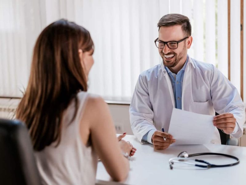 Médico atencioso com prontuário em atendimento humanizado a paciente.