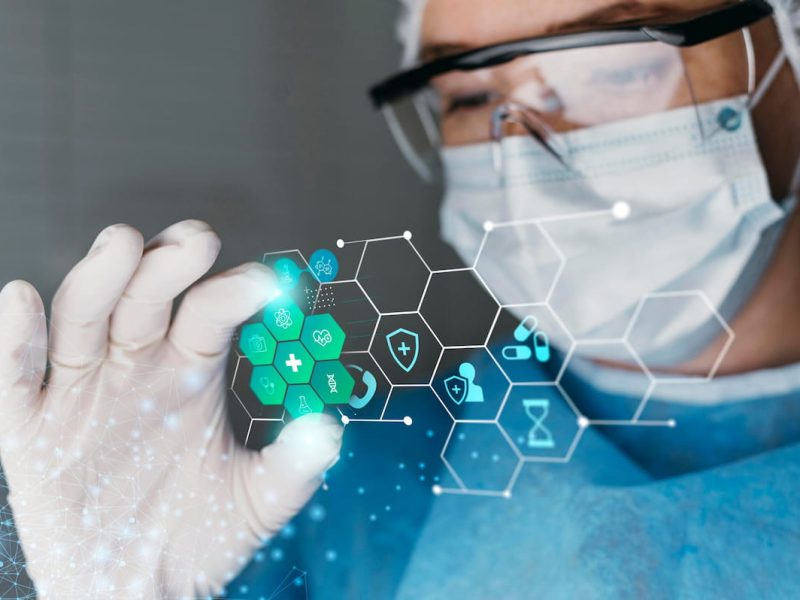 Médico de óculos e máscara, trabalhando e estudando com tecnologia e biossegurança.