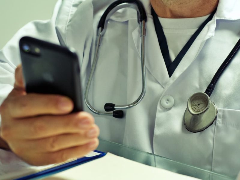 Médico com estetoscópio usando smartphone, representando branding médico e inovação na saúde.