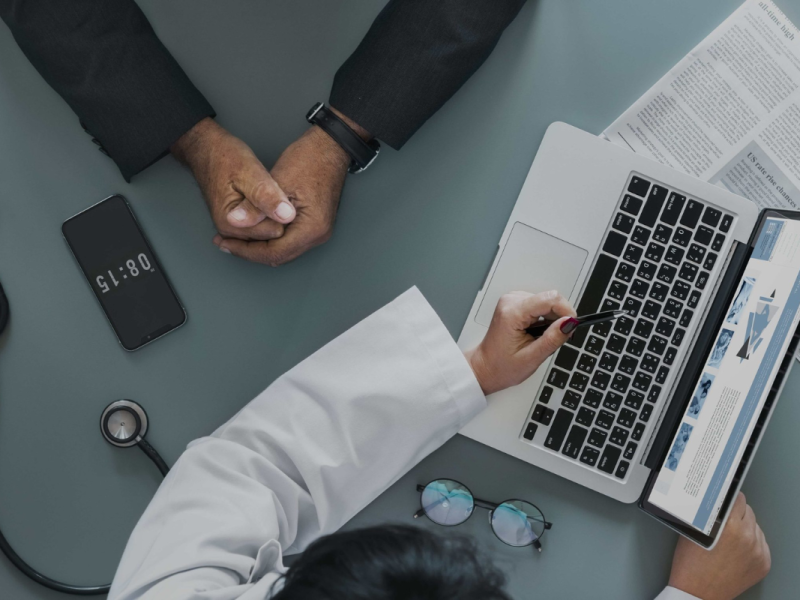 Pessoa utilizando um laptop para cadastro de pré-consulta em um ambiente com equipamentos médicos.