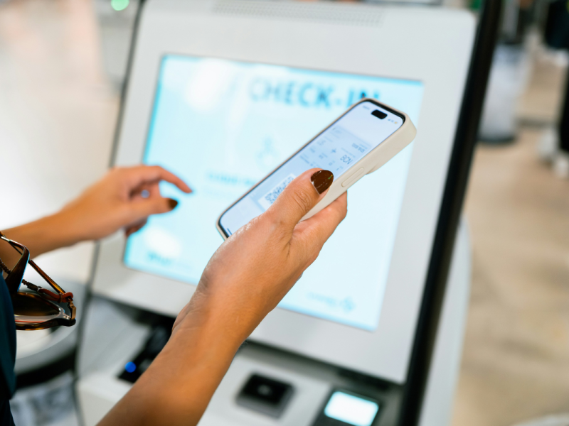 A imagem mostra uma pessoa realizando um check-in digital em um totem eletrônico.