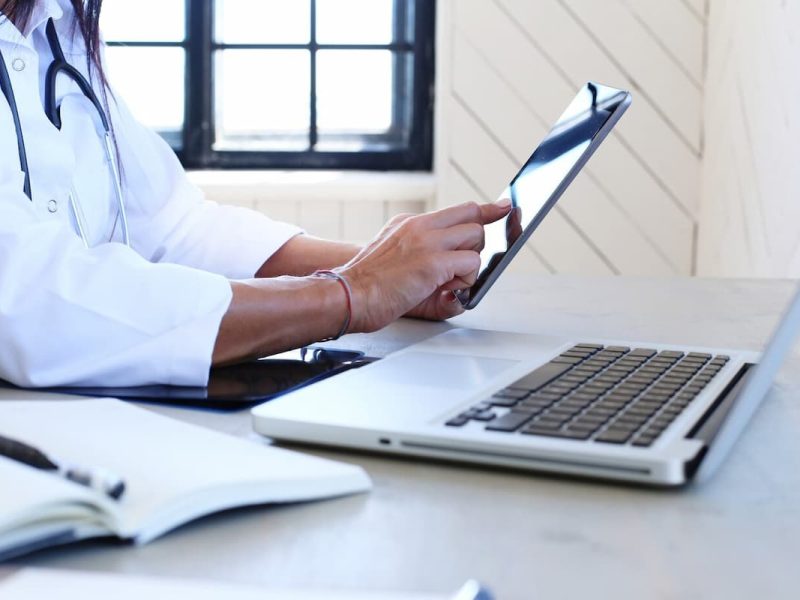 Médico analisando informações em tablet e laptop, representando a eficiência da Cobrança Inteligente do Conclínica.