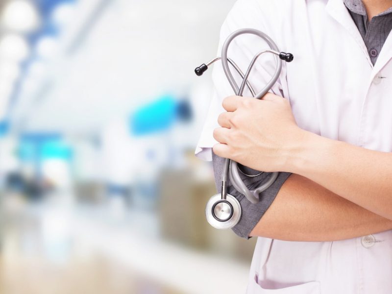 Médico com jaleco e uma blusa cinza por dentro buscando como controlar os gastos da clínica médica.
