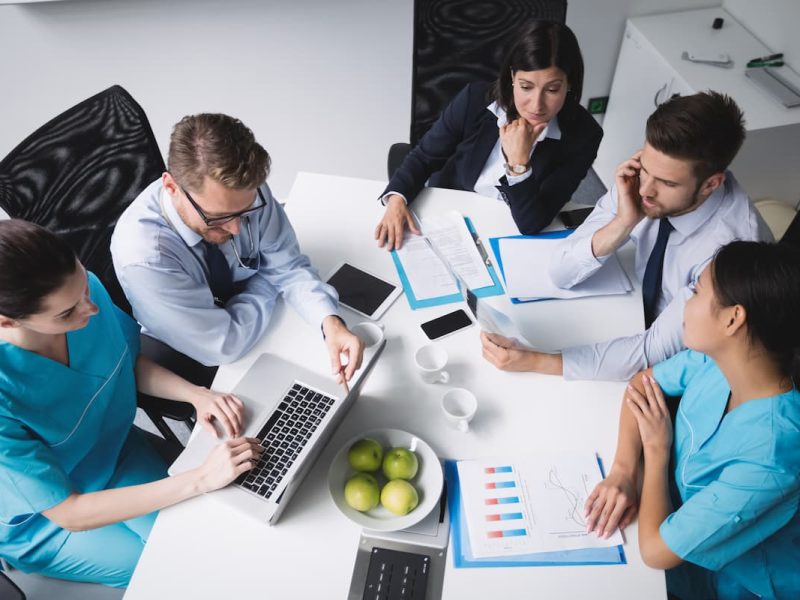 Várias pessoas ao redor de uma mesa com um laptop, conversando sobre como funciona um coworking médico.