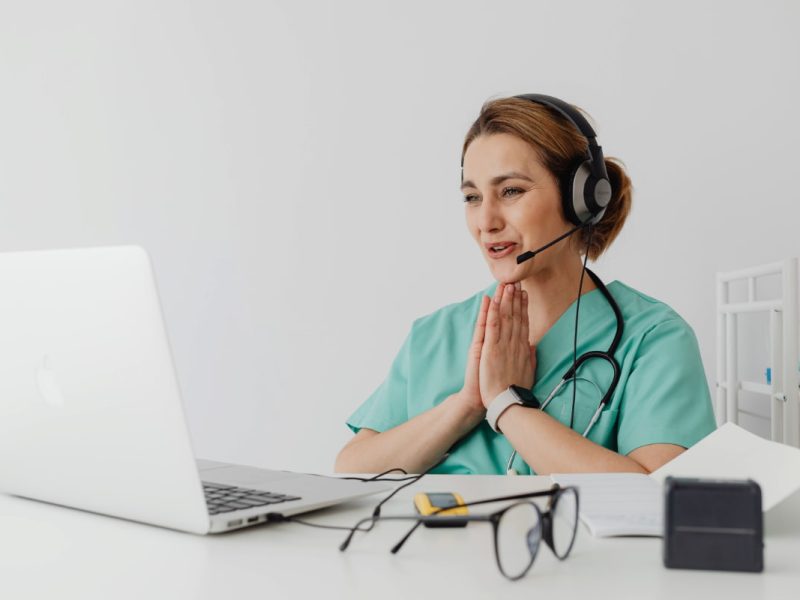 Profissional de saúde usando laptop, fone e estetoscópio, exemplificando como trabalhar com telemedicina.