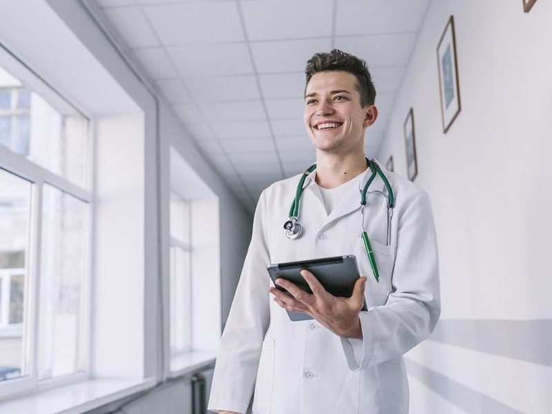 Médico sorridente com tablet na mão, fazendo uma pesquisa de como transformar o consultório em uma clínica médica.
