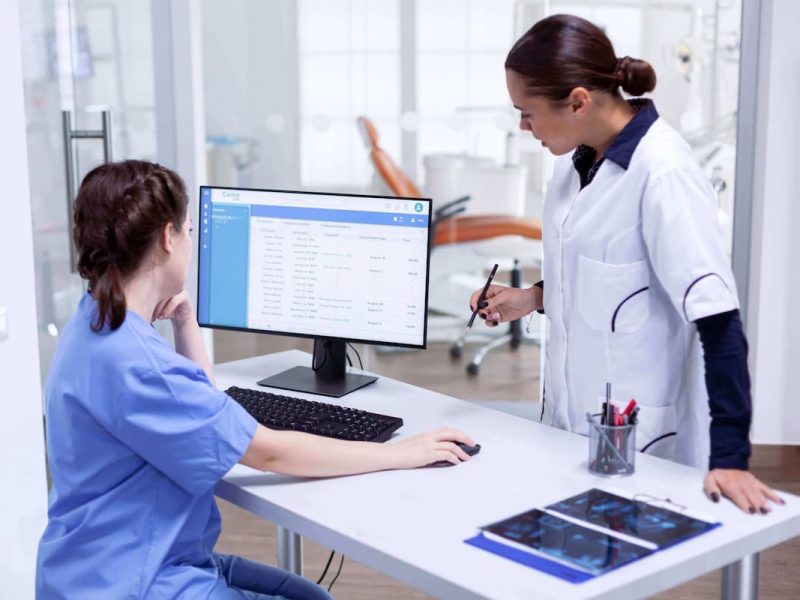 Duas profissionais de saúde fazendo confirmação de consulta médica no computador.