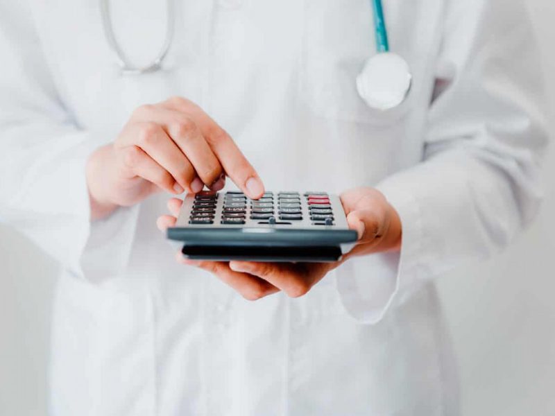 Médico segurando calculadora, simbolizando controle de fluxo de caixa na saúde.