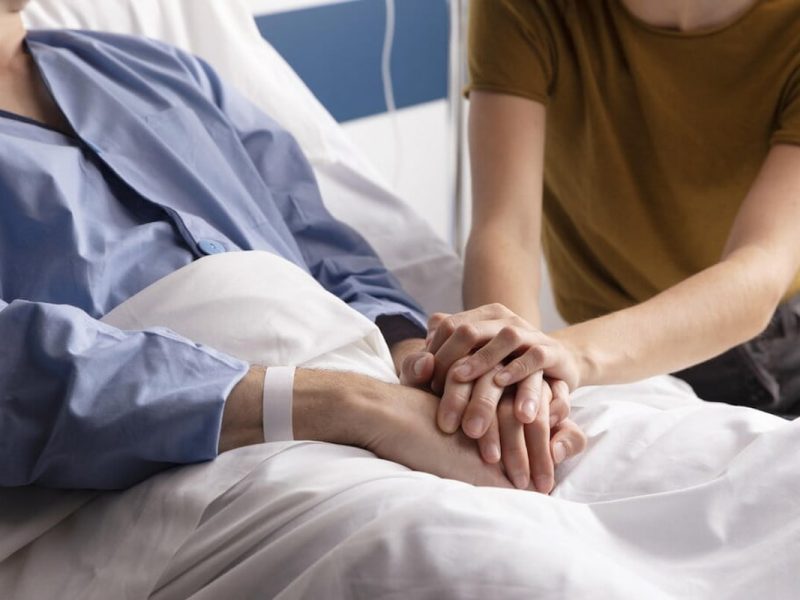 Duas pessoas juntando suas mãos apoiadas uma na outra em gesto de apoio e cuidados paliativos.