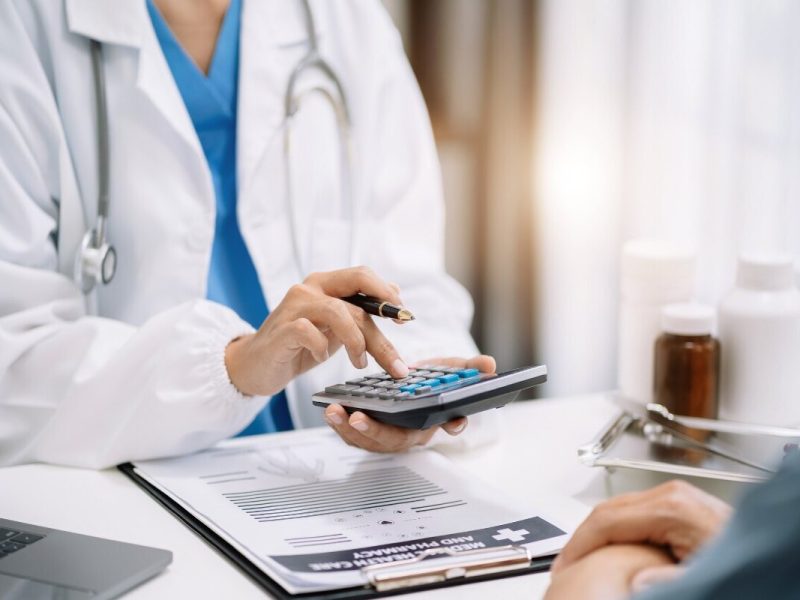 uma médica de jaleco branco faz as contas das despesas médicas para um paciente com uma calculadora