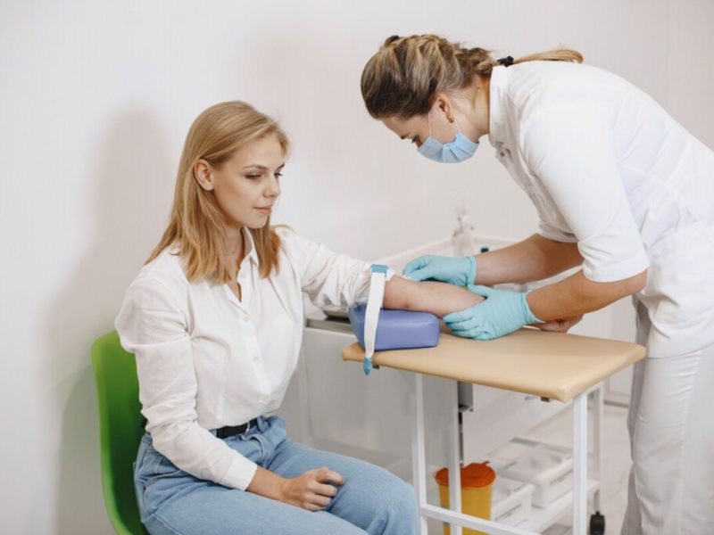 Uma mulher com o braço estendido para uma enfermeira, que conhece os direitos do paciente, fazer o exame de sangue