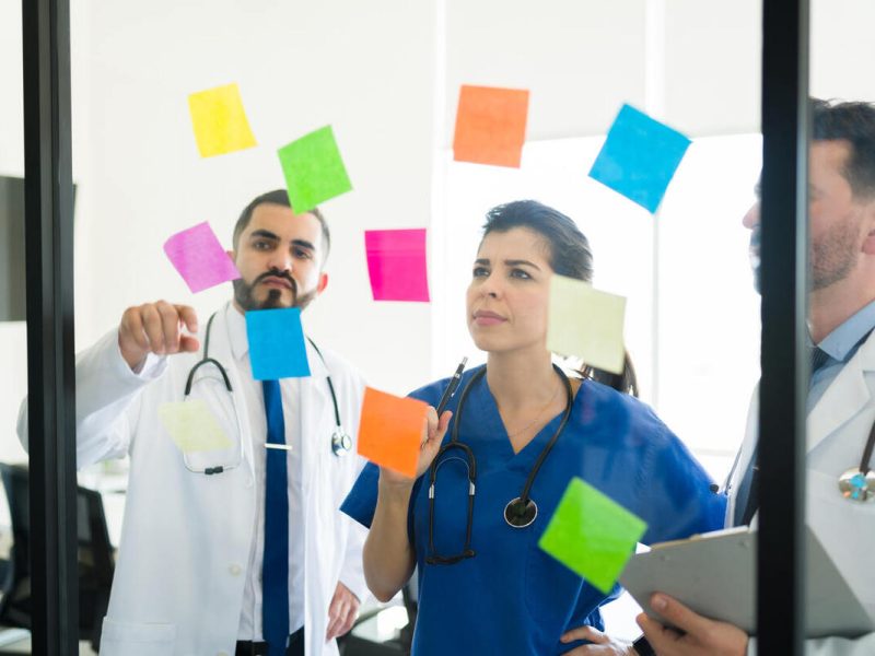 médicos analisando exemplos de empreendedorismo na área da saúde através de post its colados no vidro