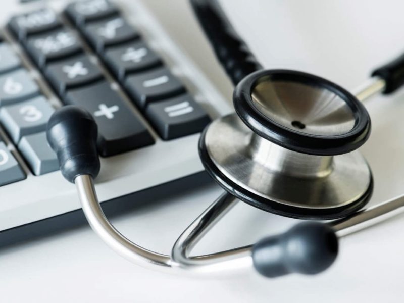 Stetoscópio, calculadora e caneta sobre uma superfície branca, simbolizando faturamento médico.