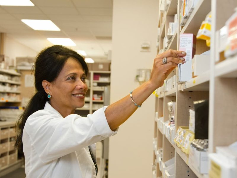 Funcionária de clínica médica organizando medicamentos nas prateleiras, representando gestão de estoque.