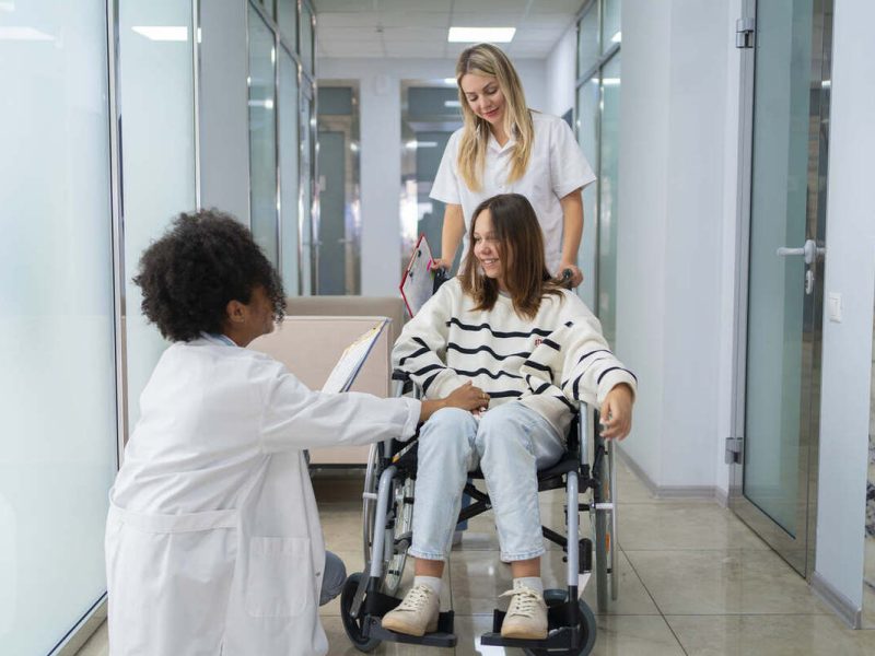 Uma médica e uma enfermeira fazem a gestão de fluxo de pacientes ao acompanhar uma na cadeira de rodas