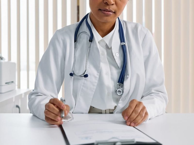 Médico com estetoscópio escrevendo em prontuário, exemplificando gestão de pessoas na clínica médica.