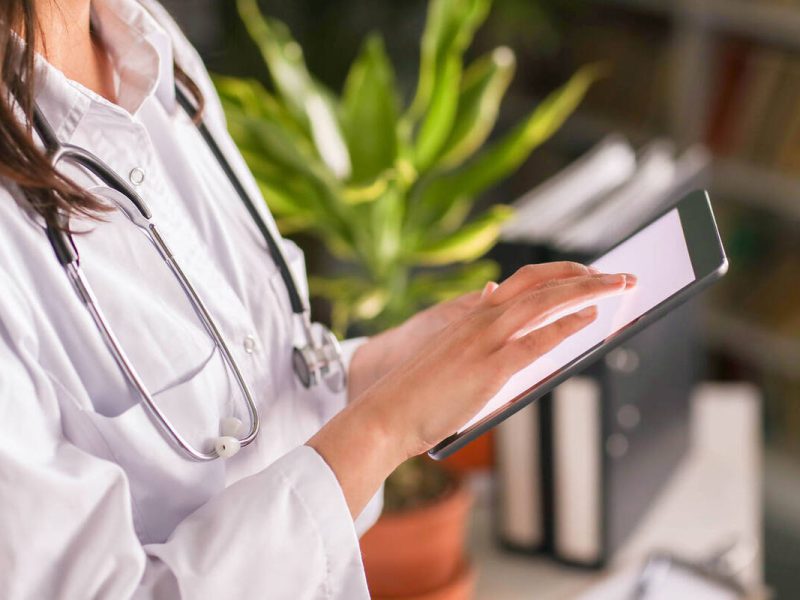 Uma médica de jaleco branco faz a gestao de planos de saúde no tablet da clínica