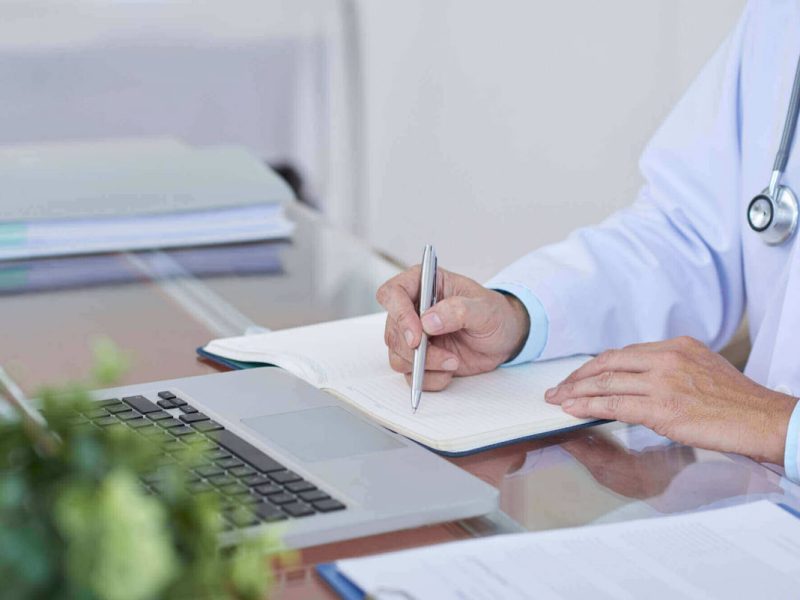 Fotografia de um médico sentado à frente de um computar e um documento impresso, preparando um recurso de glosa médica.
