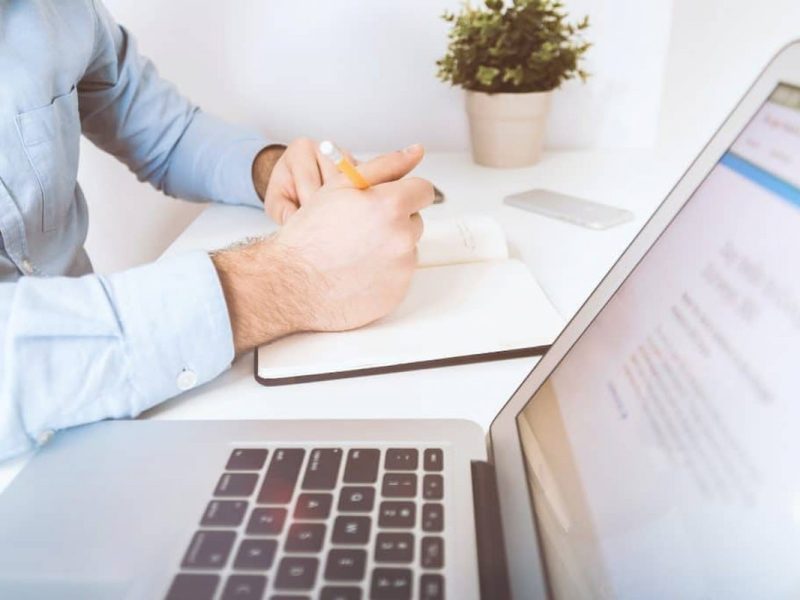 Pessoa trabalhando com laptop e guia TISS ao lado, em um ambiente de escritório claro.