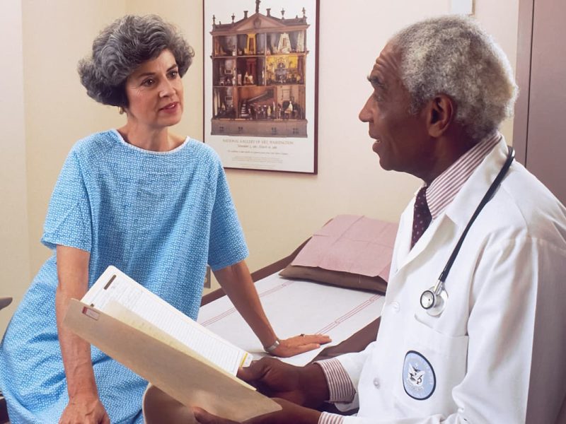 Fotografia de um médico que conversa com uma paciente no consultório médico.