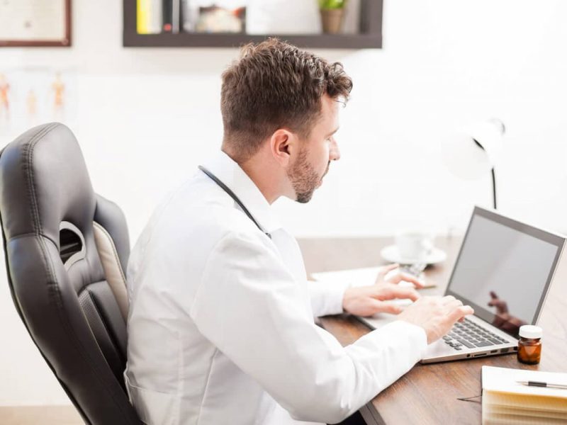 Médico trabalhando em home office com o notebook na mesa.