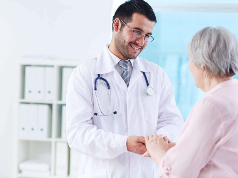 Médico segurando a mão de um paciente idoso, simbolizando cuidado e a jornada do paciente.