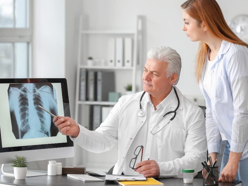 Médico explicando radiografia a paciente em consulta, ilustrando a jornada do paciente no diagnóstico e acompanhamento médico.