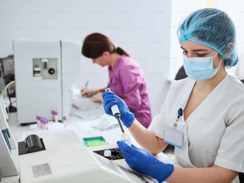 A imagem retrata duas pessoas em um ambiente que parece ser um laboratório de análises clínicas ou de pesquisa.
