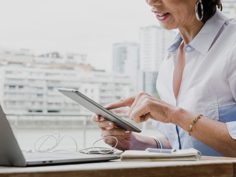 Mulher utilizando tablet ao lado de um laptop, representando tecnologia e agilidade na emissão de laudos a distância.