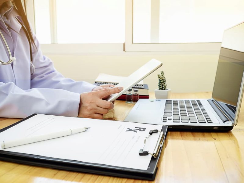 Médica com tablet e notebook, criando um lembrete de consulta médica para pacientes.