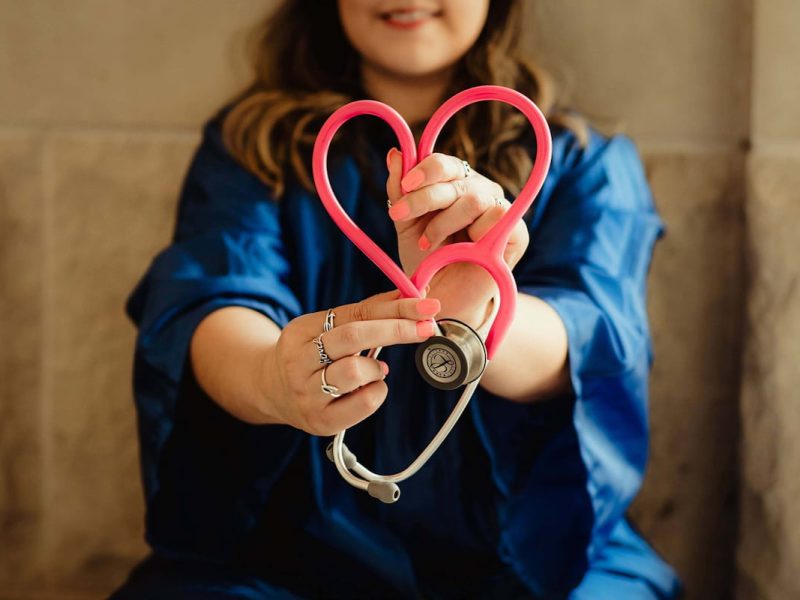 Pessoa em uniforme médico azul segurando um estetoscópio rosa em formato de coração, simbolizando a medicina moderna.
