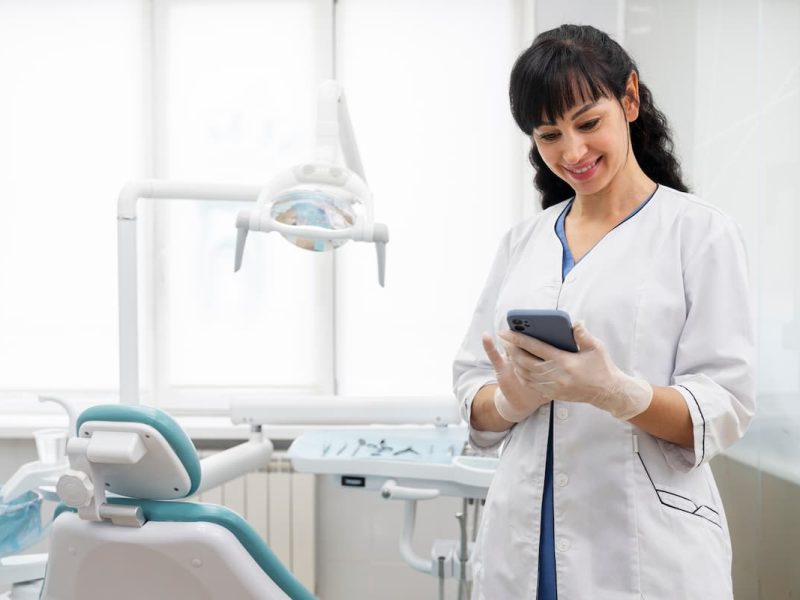 Dentista usando o melhor software para clínicas odontológicas no celular, em um consultório moderno e bem equipado.