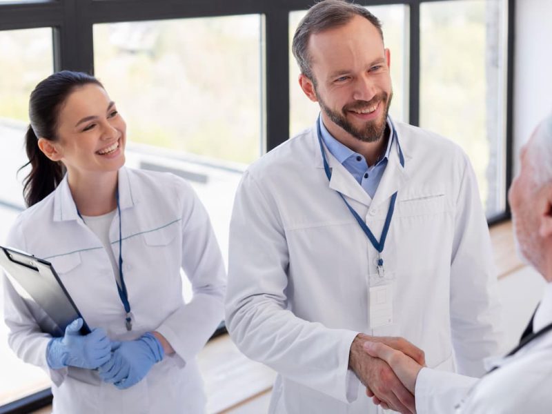 Médico cumprimentando duas pessoas, simbolizando uma negociação em saúde e colaboração profissional.