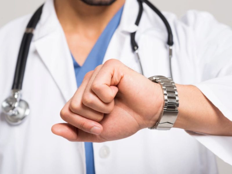 Médico verificando o relógio, representando o impacto do no-show em clínica médica devido à ausência de pacientes agendados.