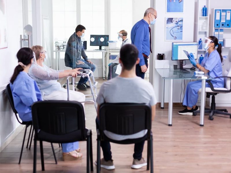 Recepção de clínica organizada com pacientes aguardando e funcionários trabalhando, exemplificando organização eficiente.