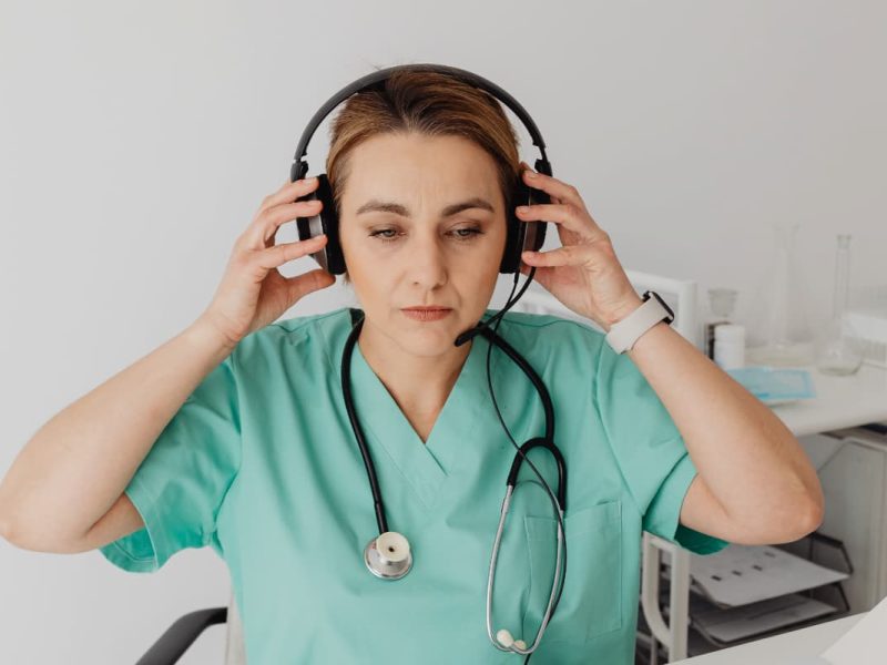 Médica com estetoscópio e fones de ouvido, preparando-se para ouvir um podcast de medicina.