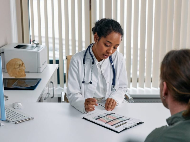 Médica analisando os princípios da bioética e os resultados de exames do paciente com uma prancheta em sua mesa.