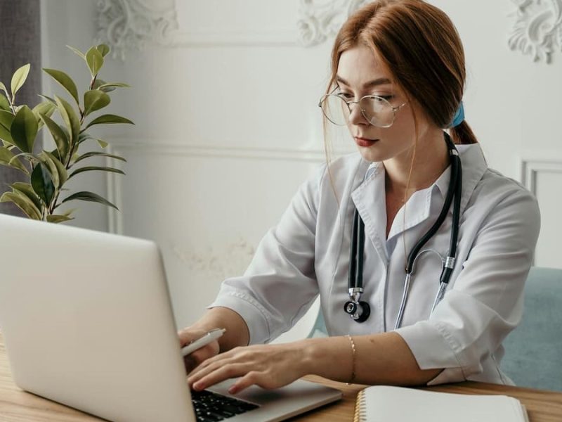 Fotografia de uma médica analisando o prontuário eletrônico de um paciente em seu notebook.
