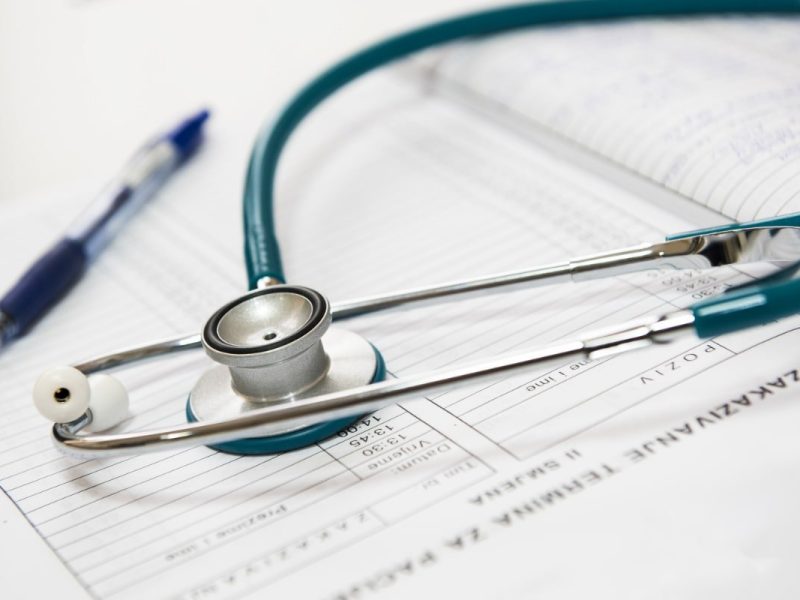 Consulta médica com receita branca: Estetoscópio e caneta sobre um recibo médico branco, com data, hora e nome do paciente.