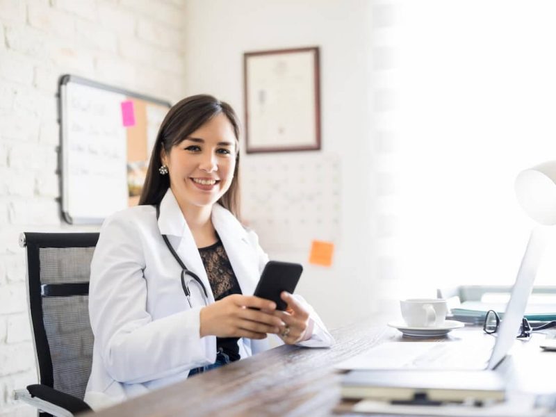 Médica consultando smartphone em escritório, simbolizando redes sociais para médicos.